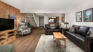 A living room with a TV, two sofas, a coffee table, and a staircase leading to a kitchen.