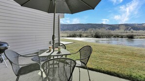 An outdoor patio with a table and chairs, a large umbrella, and a view of a river and mountains.