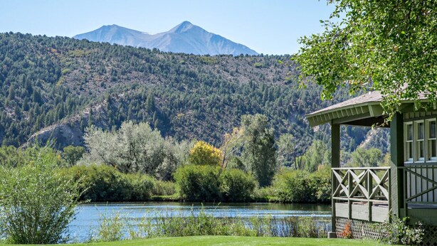 A lakeside view with a mountain in the background, a wooden gazebo, and lush greenery.