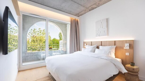 Un dormitorio moderno con una cama grande, un ventanal corredero a un balcón y una decoración minimalista.