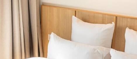 Ein ordentlich bezogenes Bett mit weißen Leinen, einem Holz-Kopfteil und einem gerahmten Bild auf einer darüberliegenden Ablage.