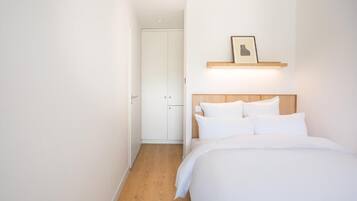 Een slaapkamer met een bed, witte muren, een houten vloer, een witte kast en een ingelijst schilderij aan de muur.