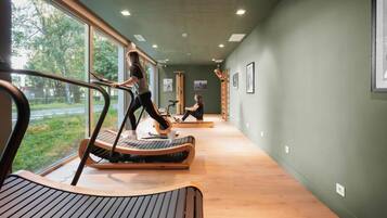 Une salle de sport équipée de tapis de course et d’appareils d’exercice, dotée de grandes fenêtres et d’un mur végétal.