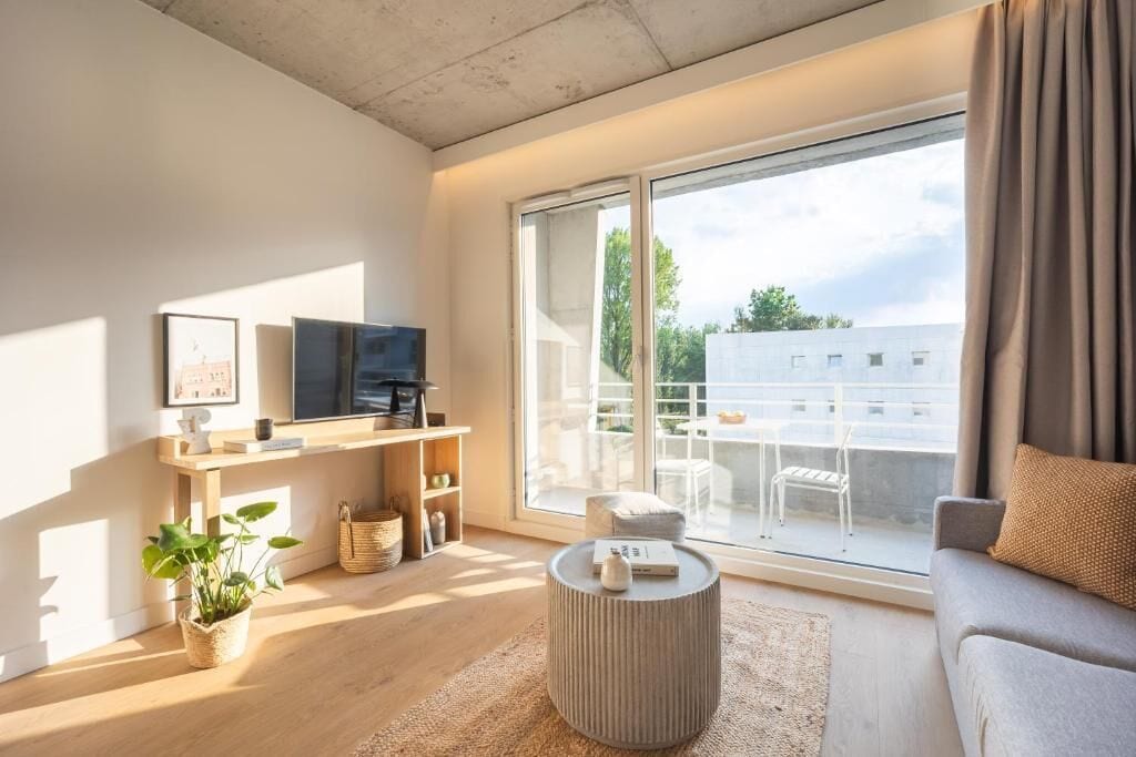 A modern living room with a large sliding glass door to an outdoor balcony, a flat-screen TV, a sofa, and a coffee table.