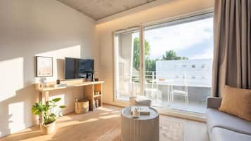 A modern living room with a large sliding glass door to an outdoor balcony, a flat-screen TV, a sofa, and a coffee table.