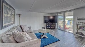 Ein modernes Wohnzimmer mit Sofa, Couchtisch, Flachbildfernseher und einem Balkon mit Blick ins Freie.