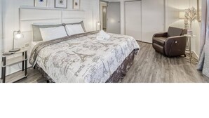 Ein Hotelzimmer mit einem großen Bett, einem Sessel, einem Schreibtisch und einem Kleiderschrank.