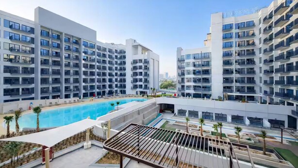 Un complex d'apartaments modern amb una piscina central, múltiples balcons i una terrassa al terrat.