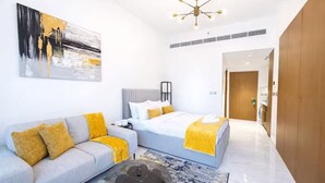 Habitació d'hotel moderna amb un sofà gris, un llit amb detalls grocs, una taula de cafè i un quadre a la paret.