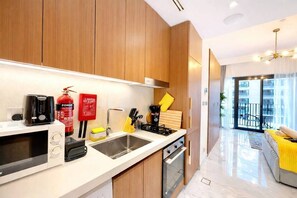 A modern kitchen with wooden cabinets, a microwave, a stove, and a sink. There is a fire extinguisher on the wall and a yellow towel hanging on the oven handle. - Your studio getaway at Azizi Beach Oasis (Dubai)