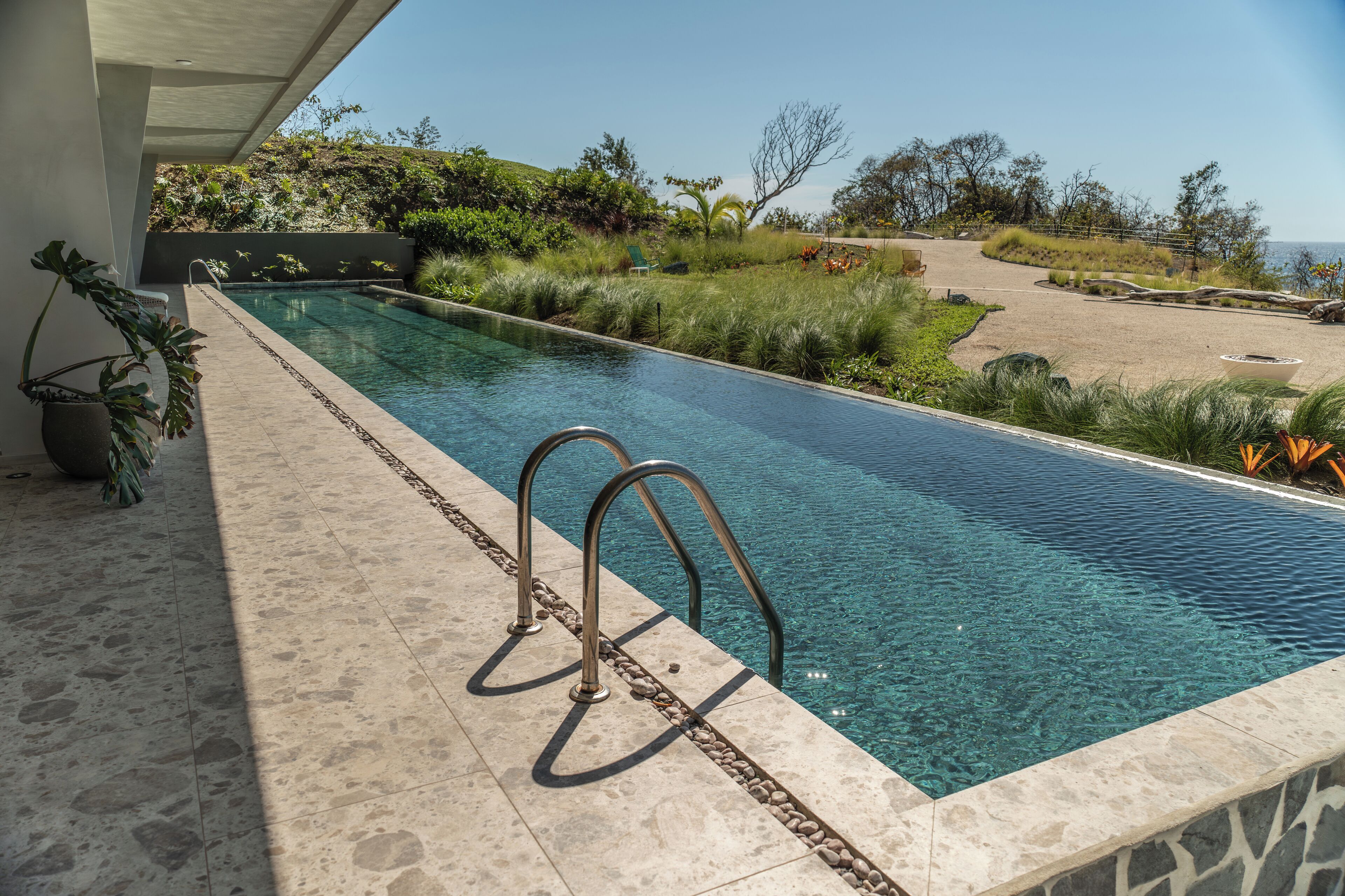 A rectangular swimming pool with clear water, surrounded by a stone deck and metal railings.