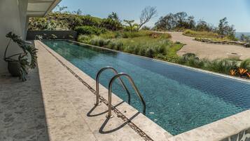 A rectangular swimming pool with clear water, surrounded by a stone deck and metal railings.