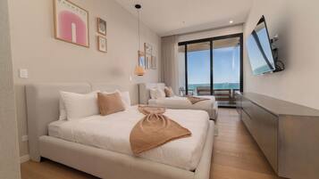 Een moderne hotelkamer met twee bedden, een grote televisie en een balkon met uitzicht op zee.