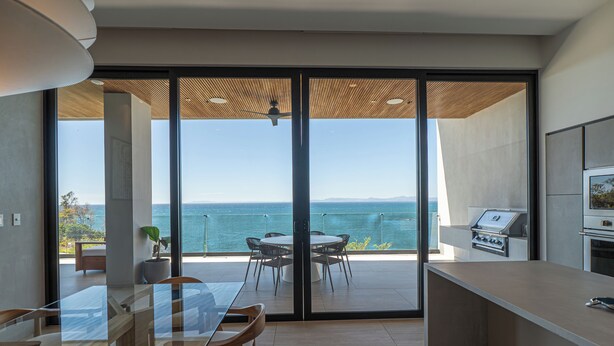 Une cuisine moderne dotée d’une grande porte-fenêtre coulissante qui donne sur un balcon offrant une vue sur la mer.
