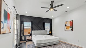 Ein modernes Schlafzimmer mit einem großen Bett, einem Deckenventilator und Kunstwerken an den Wänden.