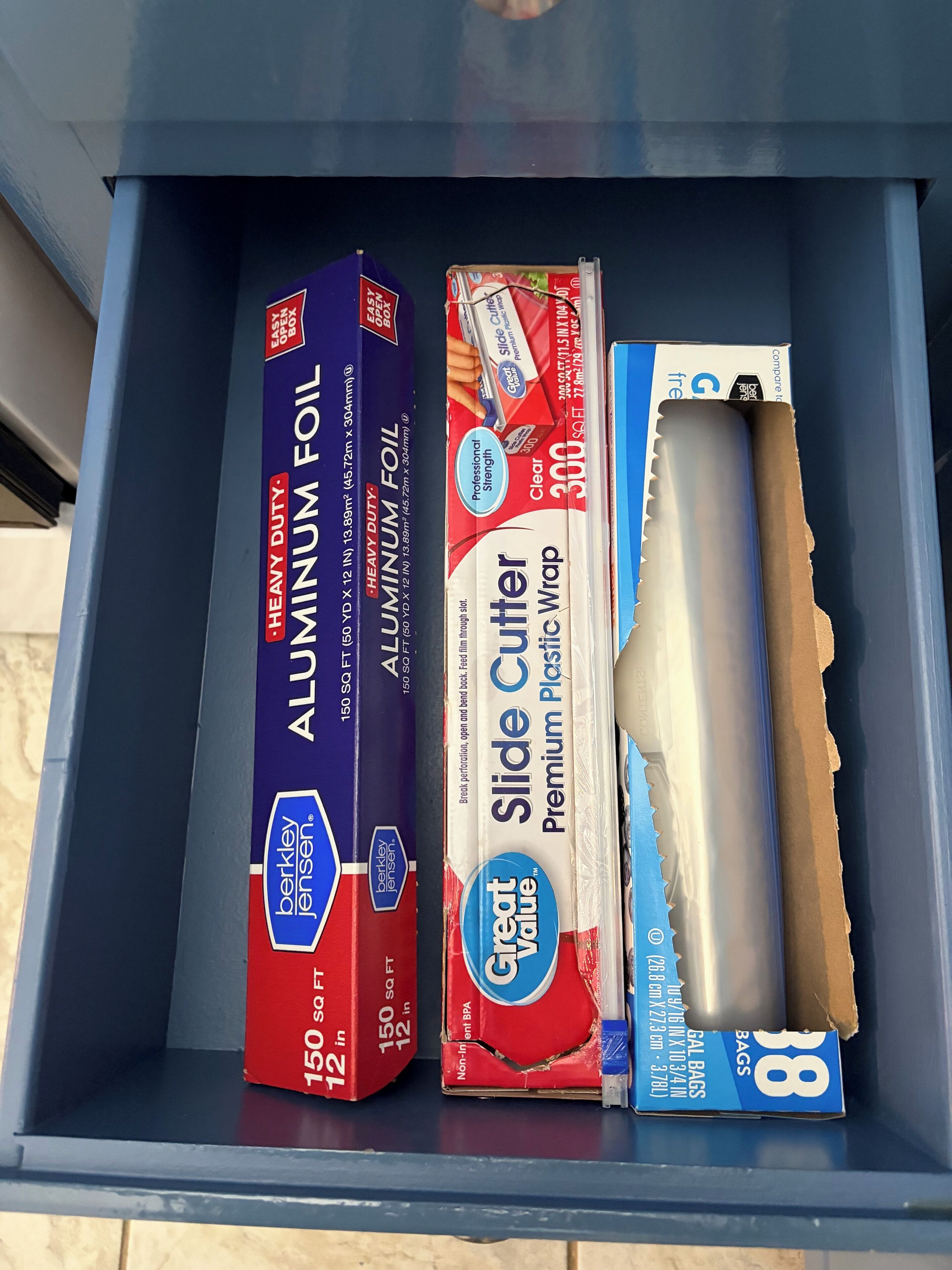 A drawer containing aluminum foil, a slide cutter, and a roll of plastic wrap.