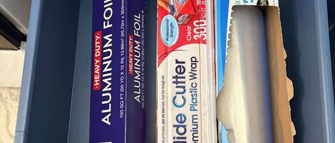 A drawer containing aluminum foil, a slide cutter, and a roll of plastic wrap.
