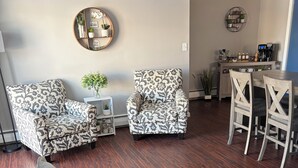 Ein modernes Wohnzimmer mit einer schwarzen Ledersofa, gemusterten Sesseln und einem Essbereich mit Holzbänken.