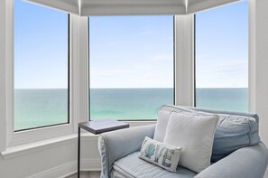 Ein Zimmer mit Meerblick durch große Fenster, ein hellblaues Sofa und ein kleiner Tisch.
