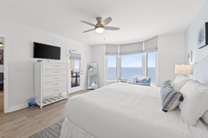 Ein modernes Schlafzimmer mit einem großen Bett, einem Deckenventilator, einem Fernseher und Meerblick.