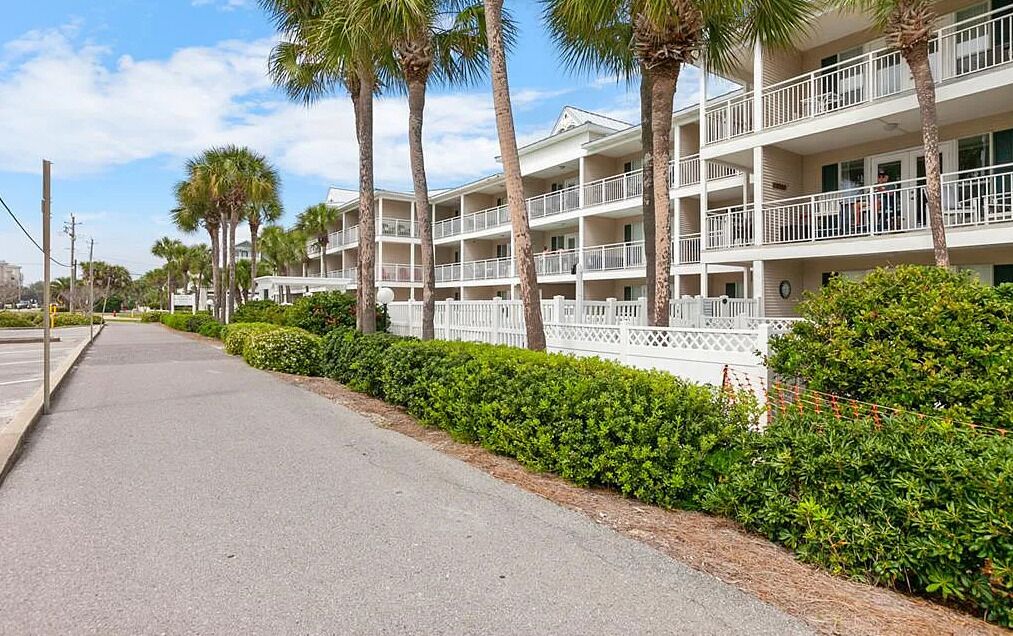 A multi-story hotel with balconies, surrounded by palm trees and well-maintained hedges.