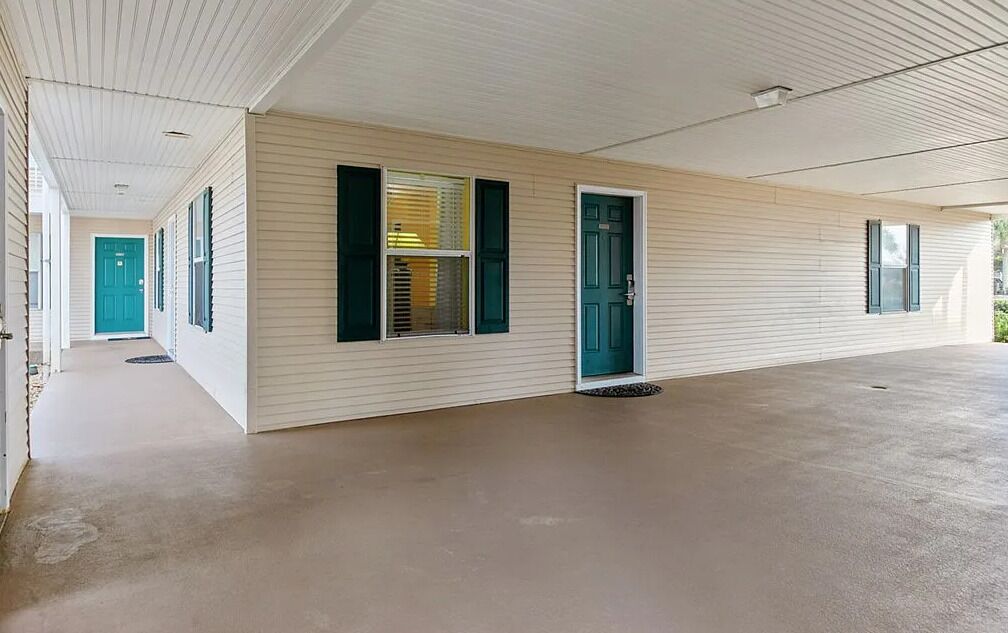 A single-story building with a covered porch, a green door, and a window with shutters.