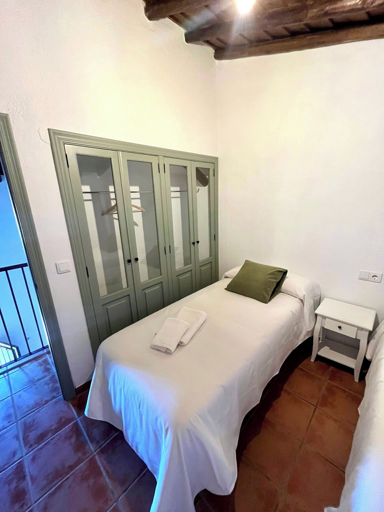A bedroom with a single bed, a nightstand, a green wardrobe, and a balcony door.
