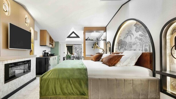 Ein modernes Hotelzimmer mit einem großen Bett, einem Flachbildfernseher, einer Küchenzeile und einem Esstisch.
