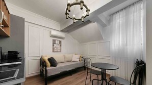 A cozy loft-style room with a sofa, a dining table, and chairs. There is a kitchenette on the left, a chandelier, and a large window with sheer curtains. - Daphne Pera ; Sakura Apart, City Center (Beyoglu)