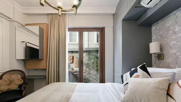 A hotel room with a bed, a TV, a chair, a window with curtains, and a balcony with plants. - Daphne Pera ; Sakura Apart, City Center (Beyoglu)