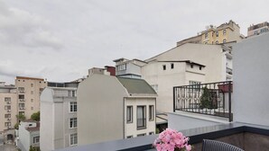 A balcony with a table and chairs, a potted plant with pink flowers, and a view of surrounding buildings. - The One Taksim 105 Room, Comfort & Privacy (Beyoglu)