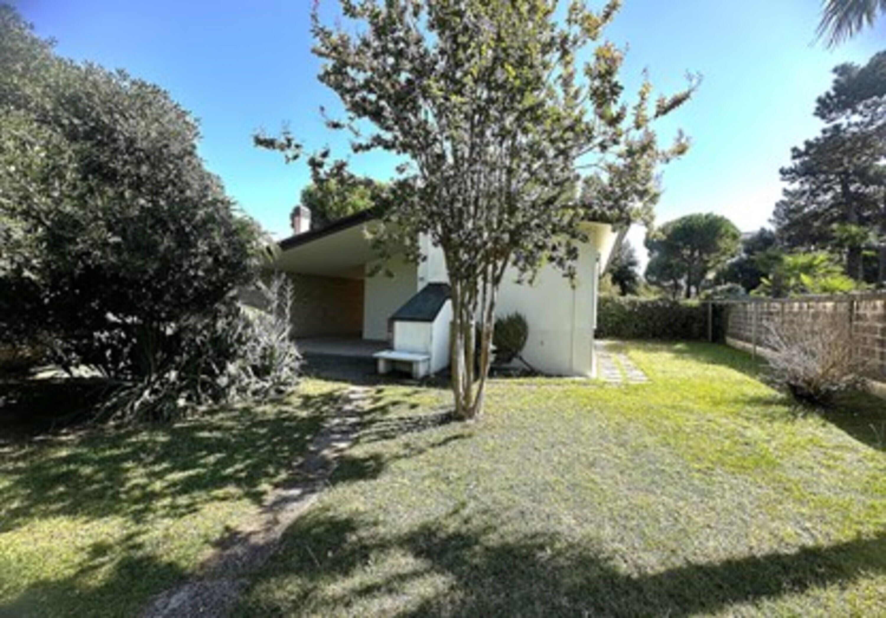 A modern house with a covered patio, a lawn, and surrounding trees.