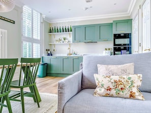 A modern kitchen with teal cabinets, a grey sofa, and a floral pillow. - Railway House (Free Gated Parking) - Platform 4 (York)