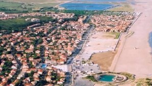 An aerial view of a coastal town with residential buildings, a beach, and a small circular water feature. - Front-line studio cabin (Fleury)