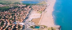 An aerial view of a coastal town with residential buildings, a beach, and a small circular water feature. - Front-line studio cabin (Fleury)