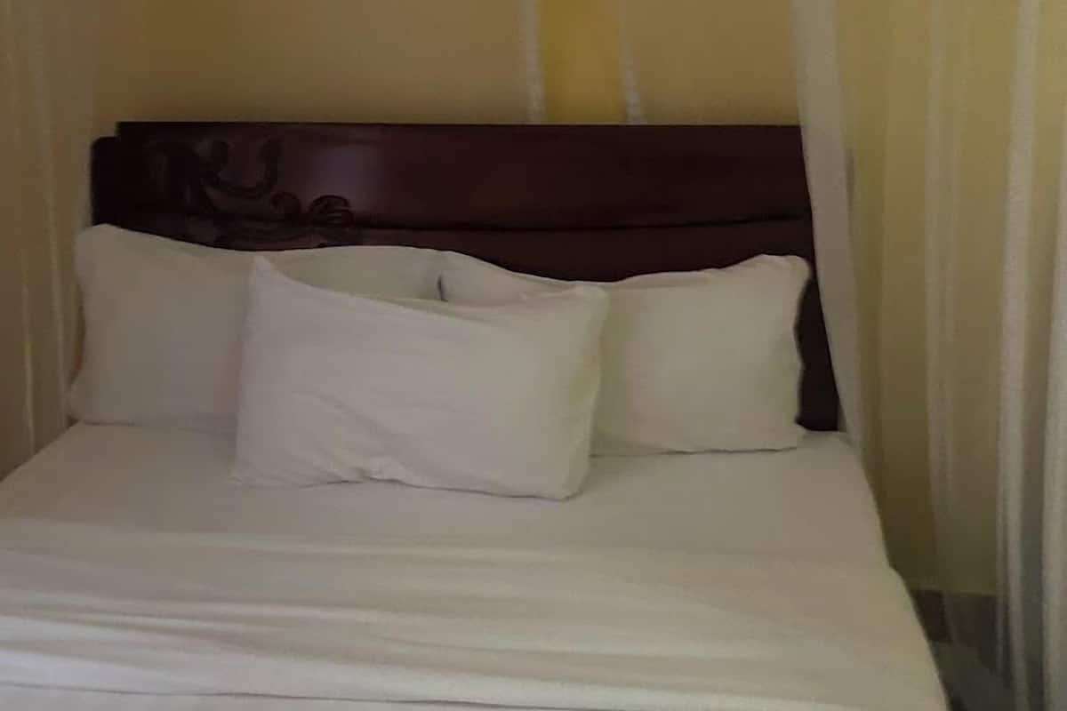 Una cama bien tendida con sábanas blancas y un cabecero de madera oscura en una habitación con paredes lisas.