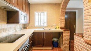 Une cuisine avec des meubles de rangement en bois, un four à micro-ondes encastré, un évier et une fenêtre.