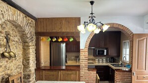 Une cuisine avec un mur en pierre, des armoires en bois, un réfrigérateur en acier inoxydable et un coin repas comprenant une table et des chaises.