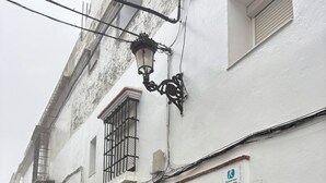 Une ruelle étroite pavée, bordée d’un immeuble blanc dont la base est en pierre, avec une porte en bois et des fenêtres grillagées.