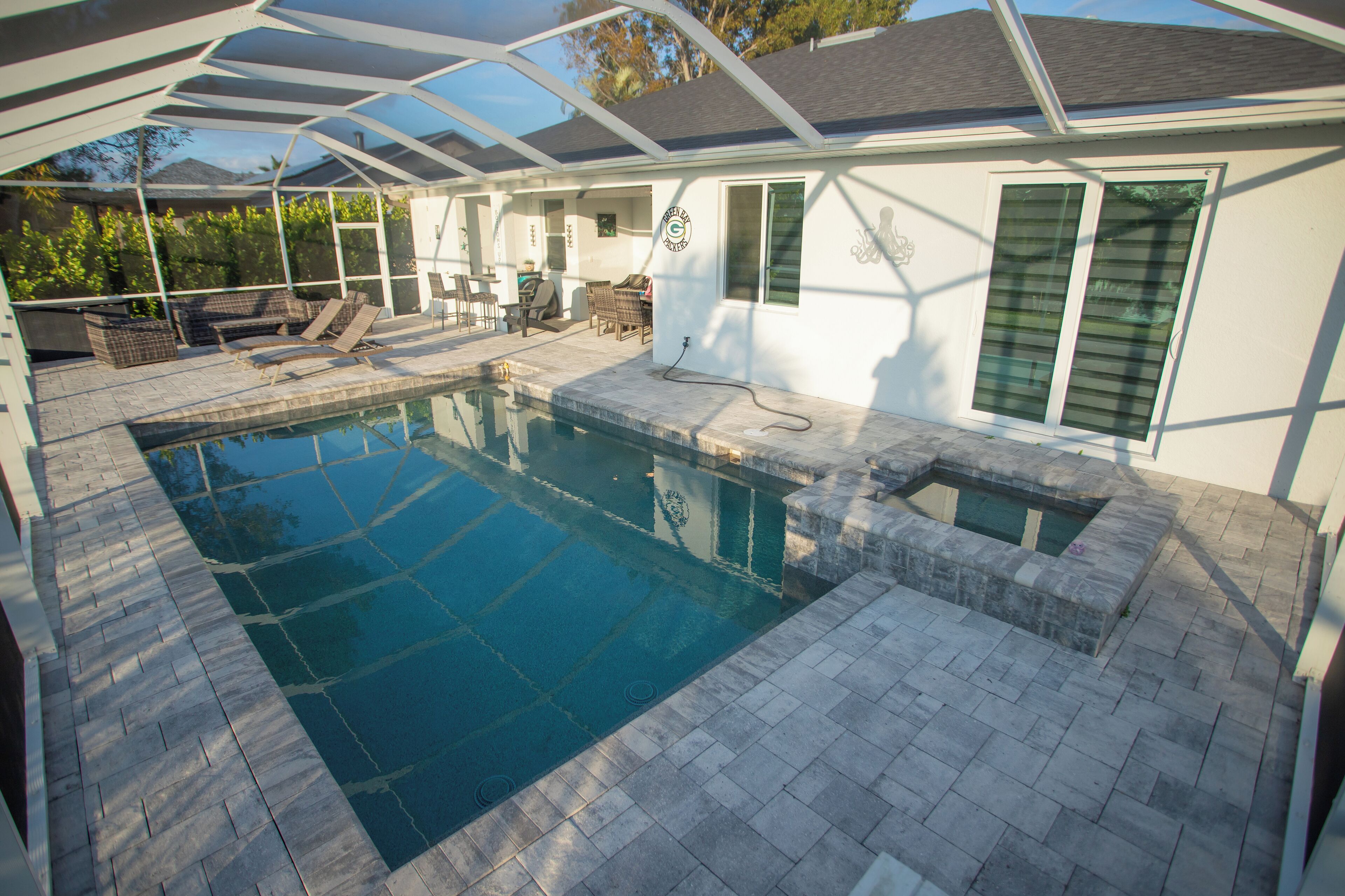 Une piscine dotée d’un patio couvert, de carreaux en pierre et d’un petit jacuzzi.