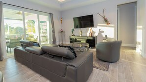 Een moderne woonkamer met een grijze bank, een ronde salontafel en een flatscreen televisie aan de muur.