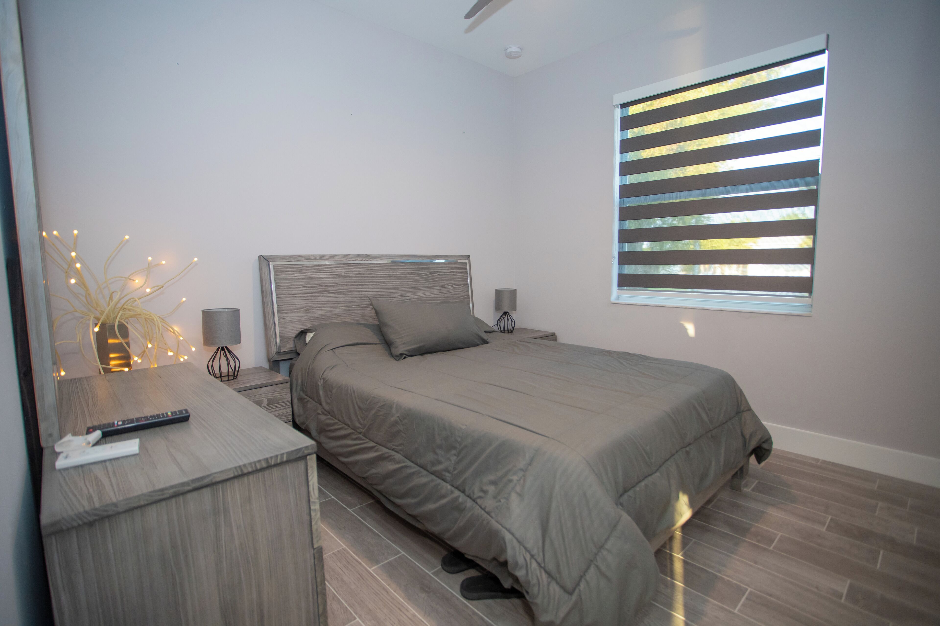 Een moderne slaapkamer met een bed, nachtkastjes, een lamp en een raam met jaloezieën.