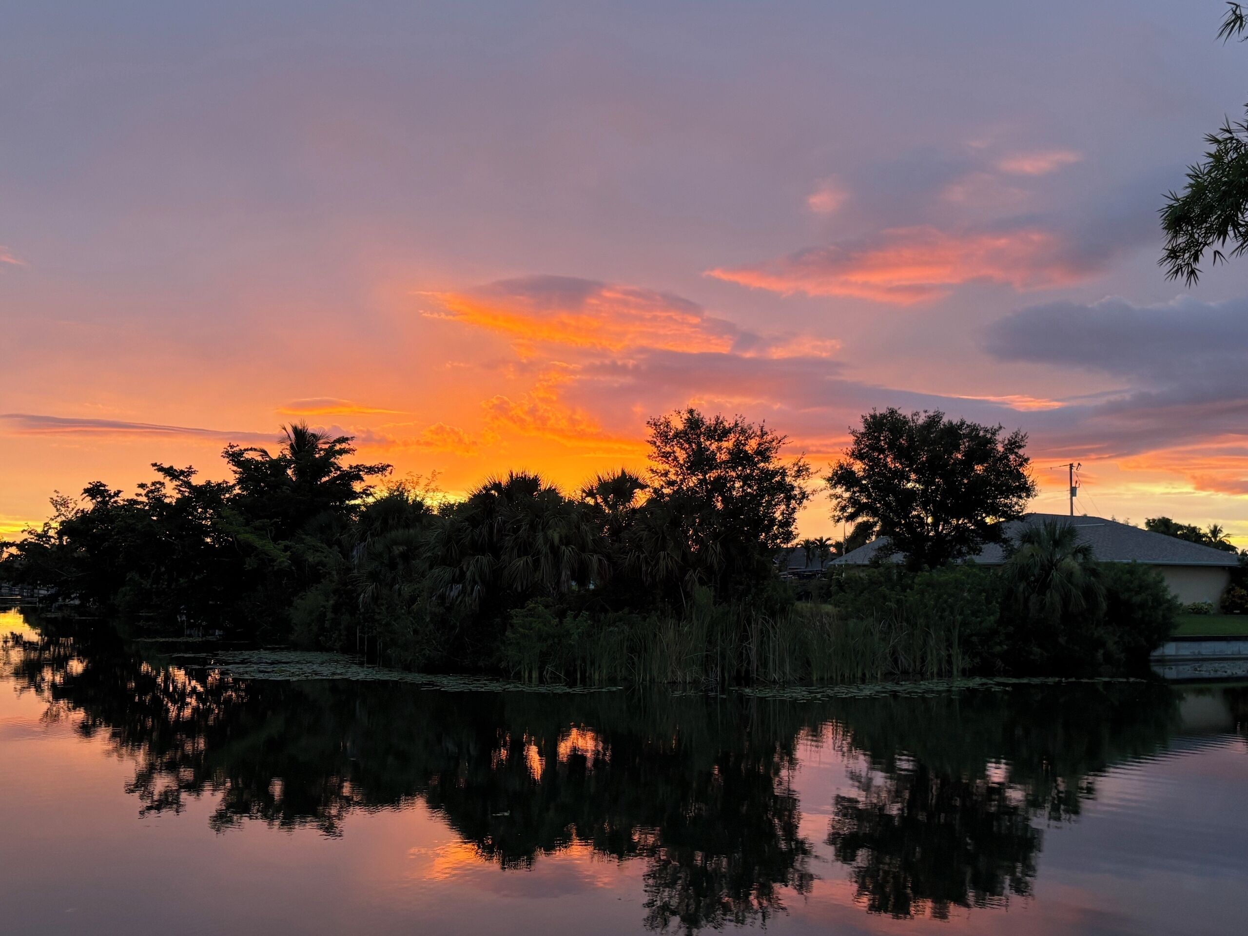 Un atardecer sobre un lago tranquilo, con árboles que se reflejan en el cielo.