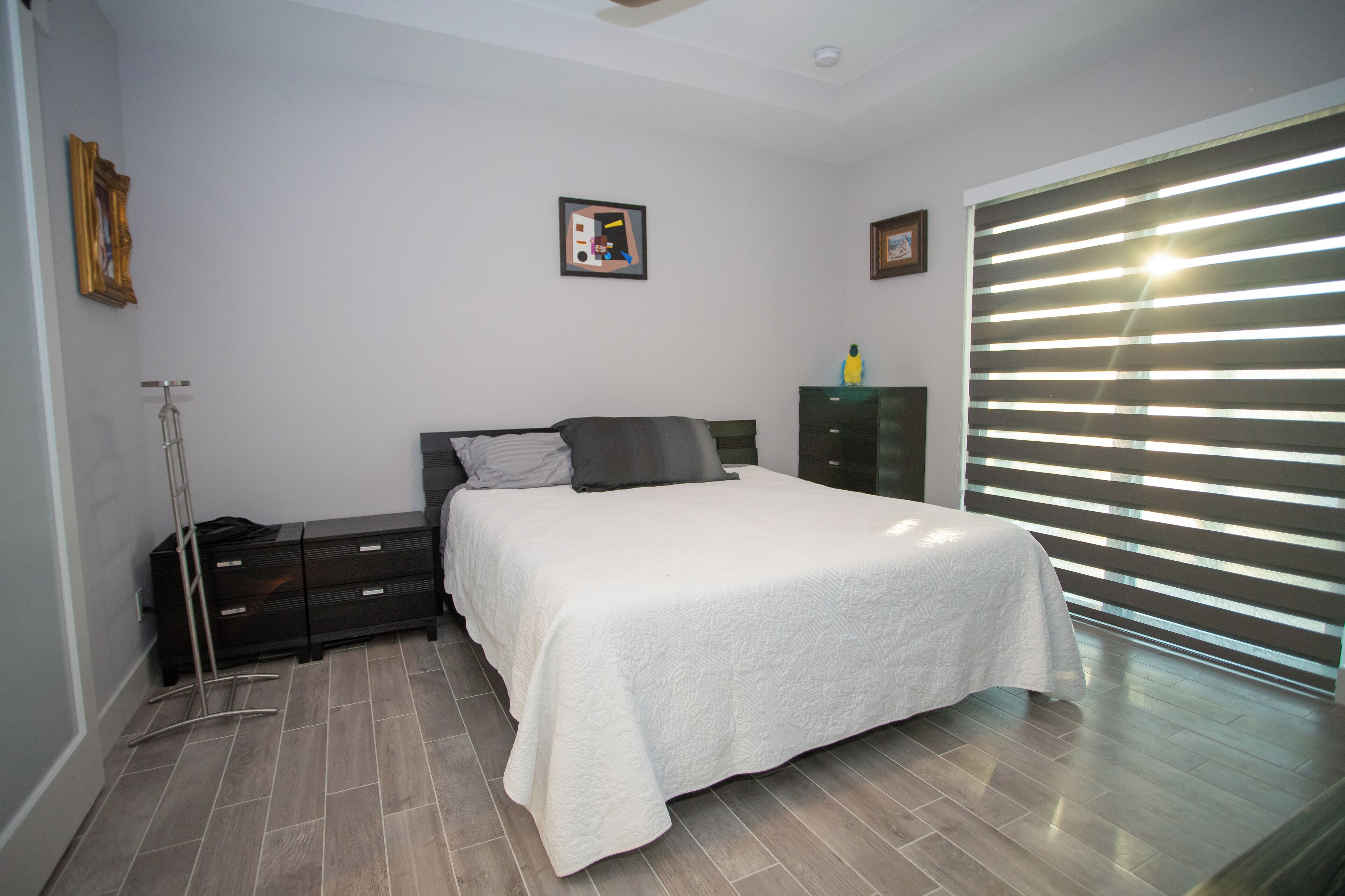 A bedroom with a bed, a dresser, a lamp, and a window with blinds.