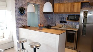 A modern kitchen with a central island, stainless steel appliances, and a patterned backsplash. - Cobertura de Alto Padrão • Cyrela • Boqueirão (Santos)