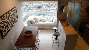 A compact kitchen with a dining area, a sofa, and a view of the city. - Cobertura de Alto Padrão • Cyrela • Boqueirão (Santos)