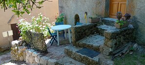 Un escalier en pierre menant Ă une porte, une table ronde avec des chaises bleues et des plantes en pot.