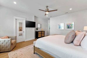 Ein Schlafzimmer mit einem Bett, einem Deckenventilator, einem Fernseher, einer Kommode und Bildern an der Wand.
