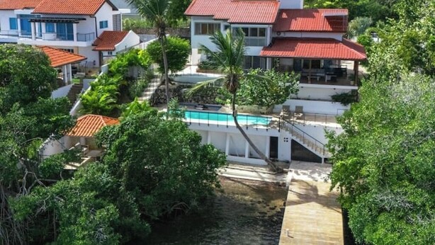 A multi-story residential building with a swimming pool, surrounded by lush greenery and palm trees. - A Casa do Lago: comfort, nature and unforgettable moments on the shore of the water (Romana)
