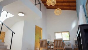 A spacious living area with a high ceiling, wooden beams, and a staircase. There are two wooden chairs and a table, a large window, and a door leading to another room. - A Casa do Lago: comfort, nature and unforgettable moments on the shore of the water (Romana)